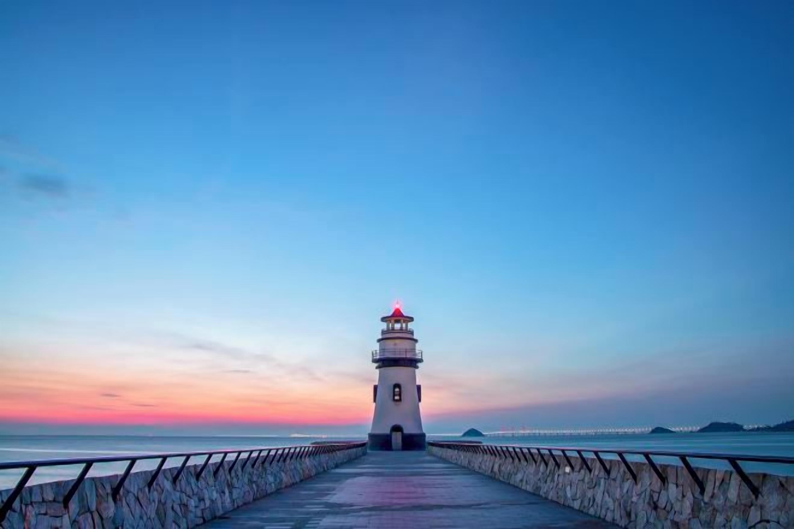 Ein Leuchtturm am Ende eines Stegpiers unter blauem Himmel.