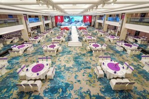 Une salle de banquet avec des rangées de tables rondes, chacune recouverte d’une nappe blanche et agrémentée de décorations florales violettes.