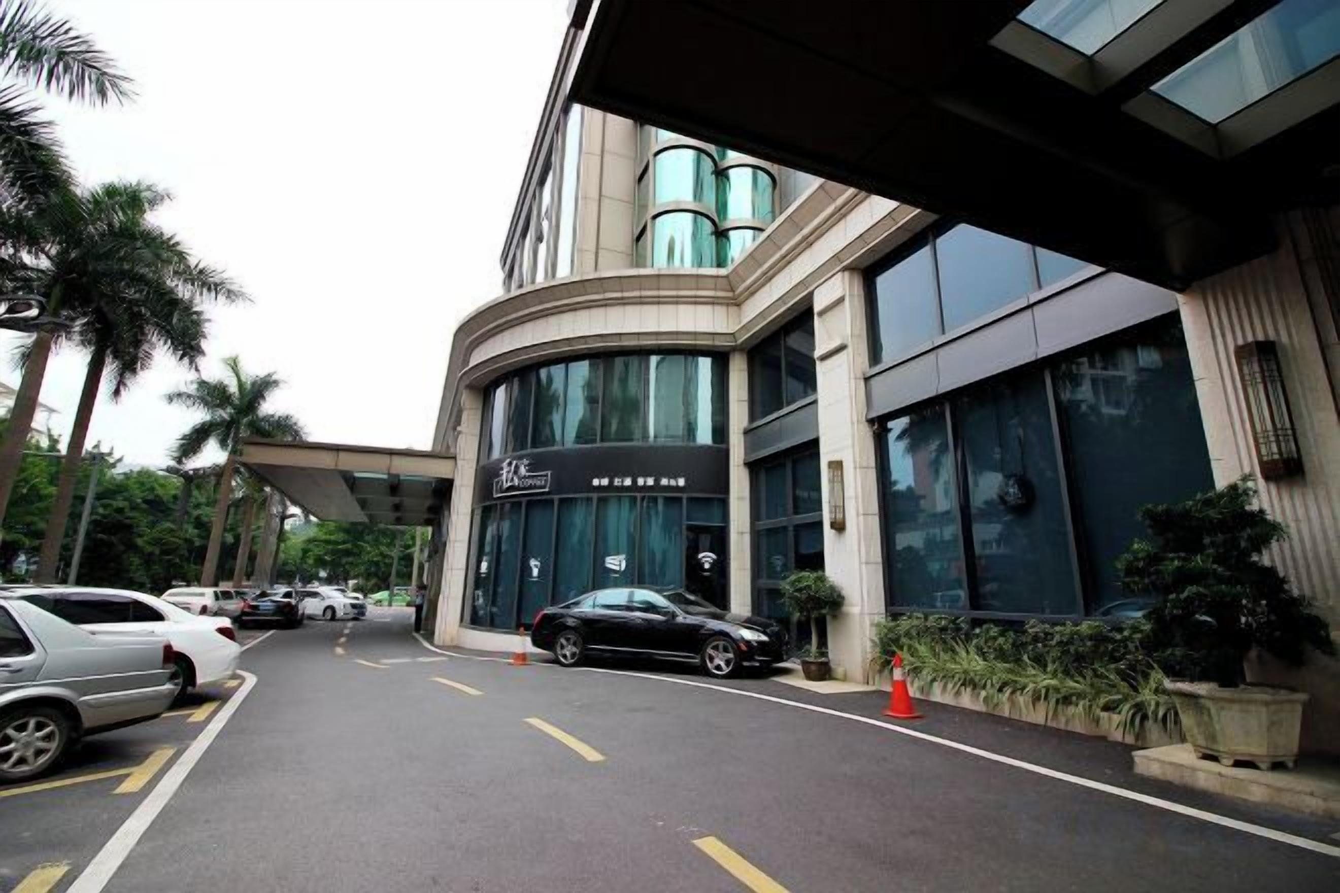 A hotel entrance with a curved facade, a car parking area, and a signboard.