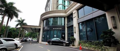 A hotel entrance with a curved facade, a car parking area, and a signboard.