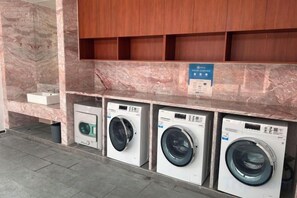 A laundry area with three washing machines and a marble wall. - Xinhaili Hotel (Zhuhai)
