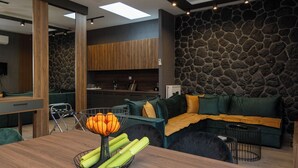 Ein modernes Wohnzimmer mit Steinwand, einem Holzespeisetisch mit Obstschale und einem grünen Sofa.