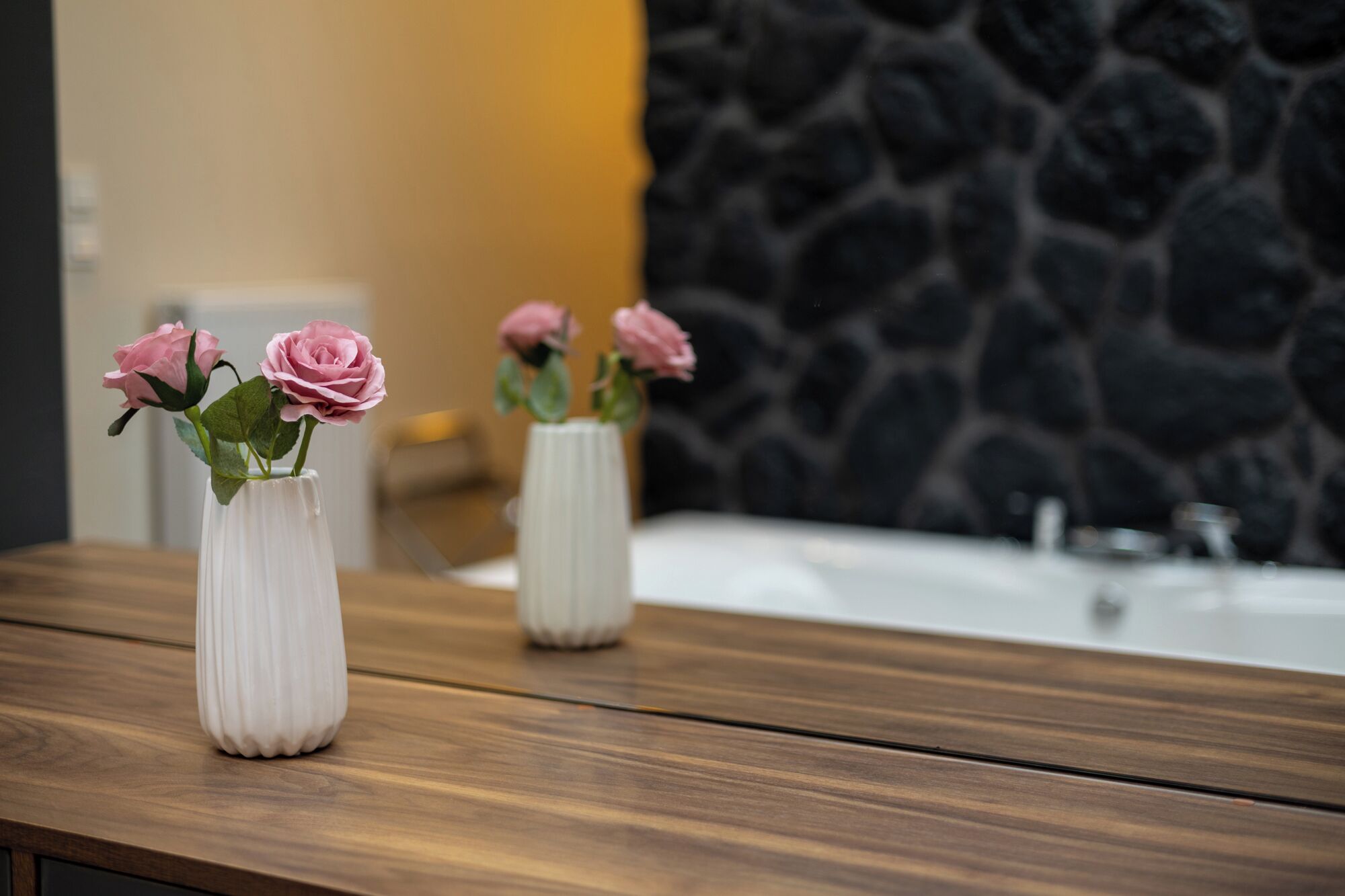 Drie witte vazen met roze rozen op een houten aanrecht.