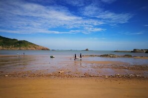Ein Strand mit felsigem Ufer, ruhigem Wasser und wolkenlosem Himmel.