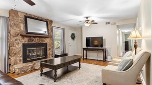 A living room with a stone fireplace, a television, a ceiling fan, and a sofa. - Pet Friendly Relaxing Retreat Walk to DT|King Bed (Cary)