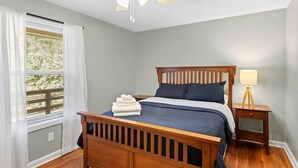 A bedroom with a wooden bed, a nightstand, a ceiling fan, and a window with blinds. - Pet Friendly Relaxing Retreat Walk to DT|King Bed (Cary)