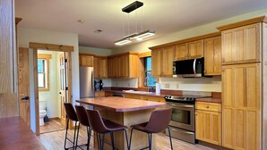 Una cocina moderna con armarios de madera, un refrigerador de acero inoxidable, un microondas y una isla grande con taburetes de bar.