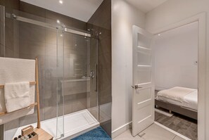 Un baño moderno con ducha de vidrio, una puerta blanca y una cama con alfombra azul.