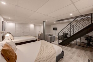Un dormitorio moderno con una cama grande, un sofá gris, una escalera y un televisor de pantalla plana.