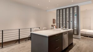 Una cocina moderna con una isla central, un comedor con sillas, horno empotrado y un amplio armario con puertas de vidrio.