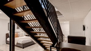 Un interior moderno con una escalera de madera que sube a un dormitorio tipo loft, un comedor y una sala de estar.