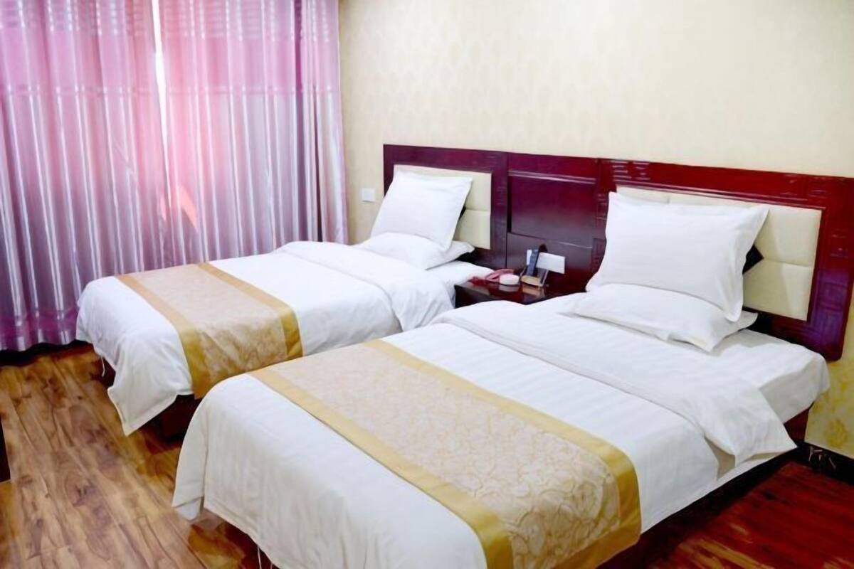 A hotel room with two beds, wooden flooring, a wooden headboard, and a curtain.