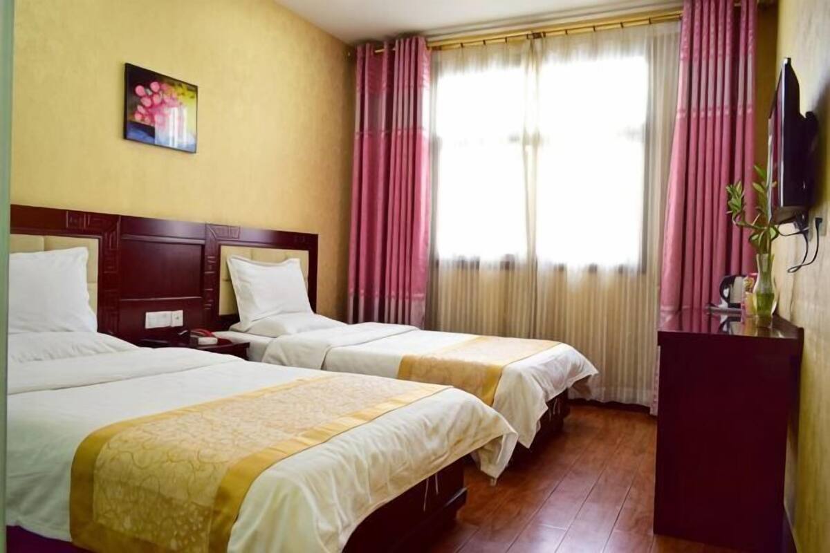 A hotel room with two beds, a wooden headboard, a television, and a window with curtains.