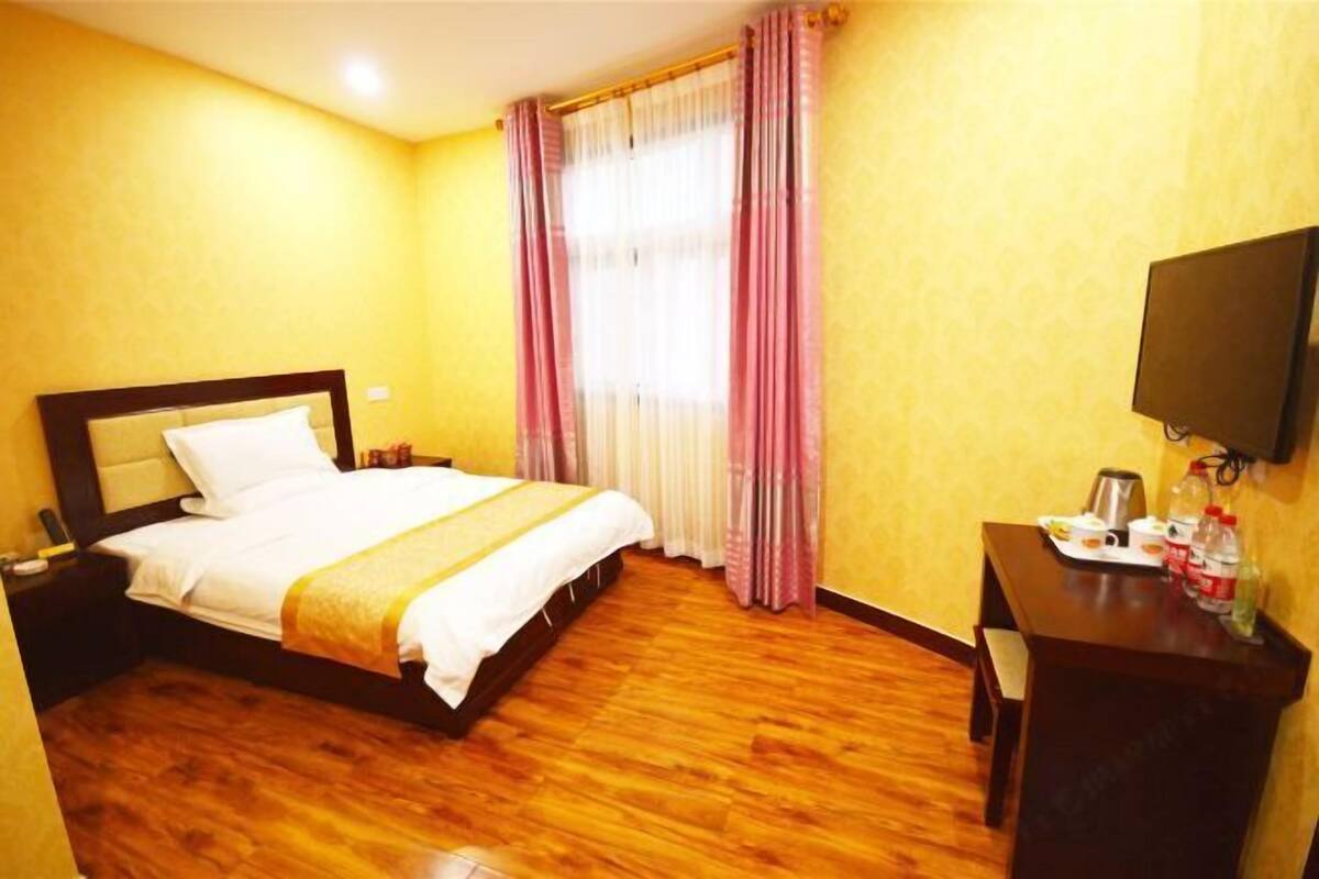 A hotel room with a bed, wooden flooring, a desk with a flat-screen TV, and a window with curtains.