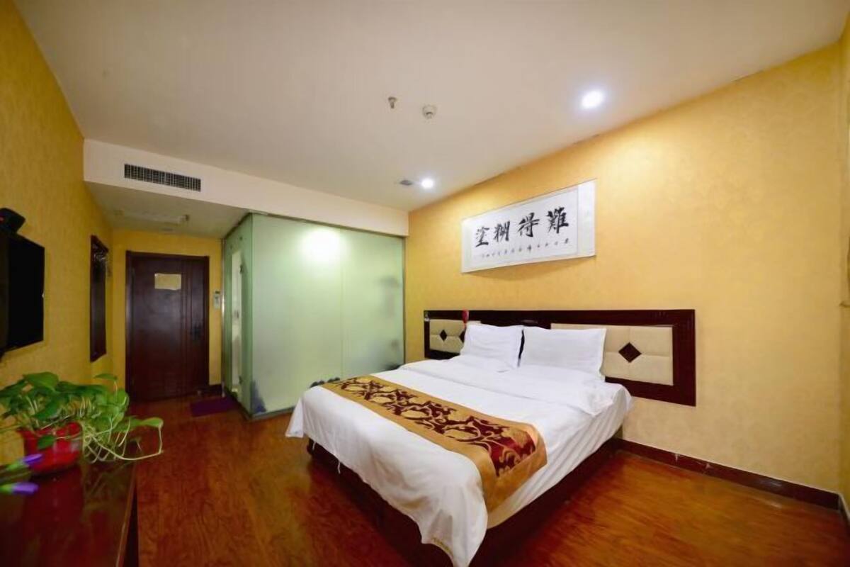 A hotel room with a bed, a wall-mounted sign, a door, and a potted plant.