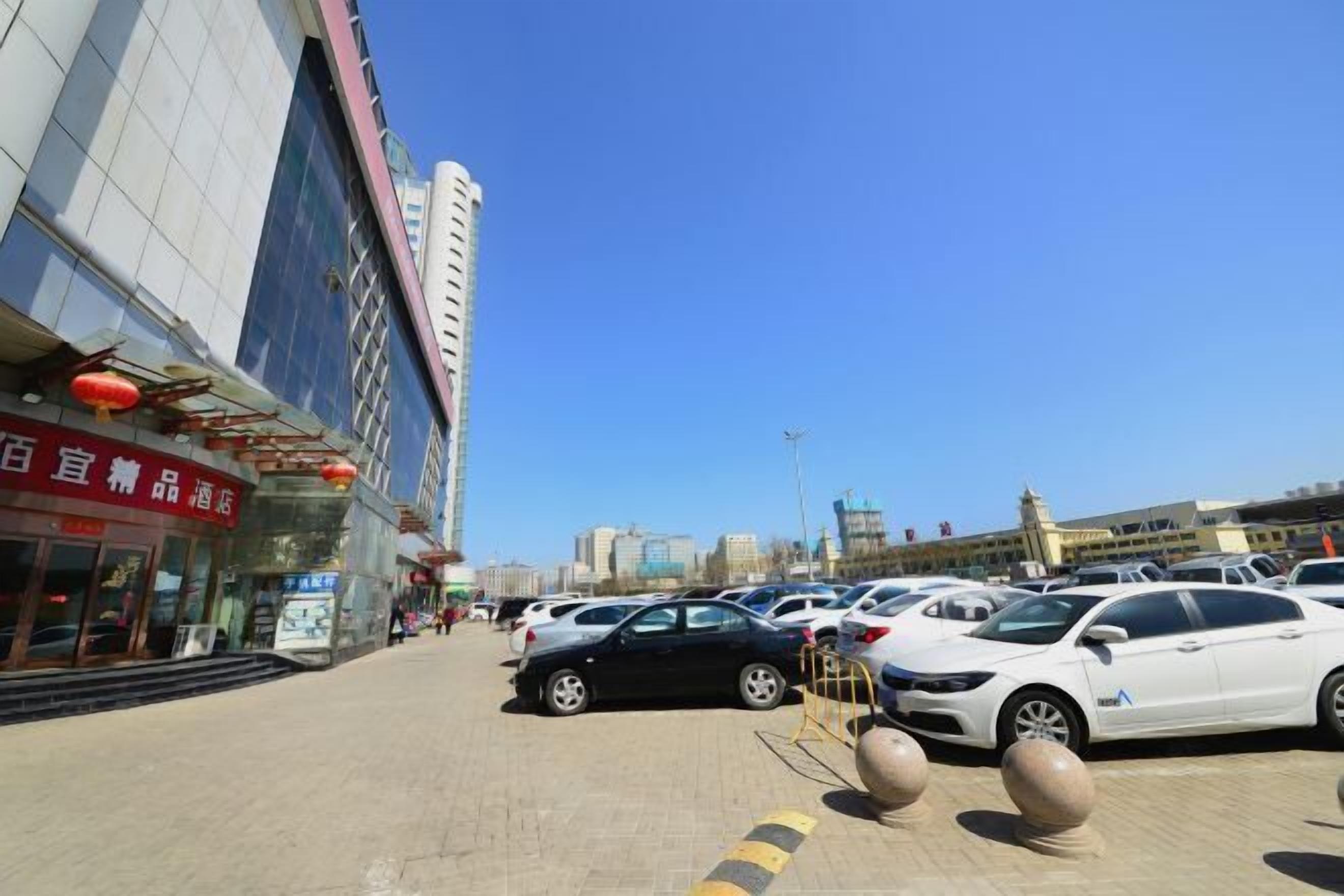 A hotel with a modern facade, a parking lot with several cars, and a clear blue sky.