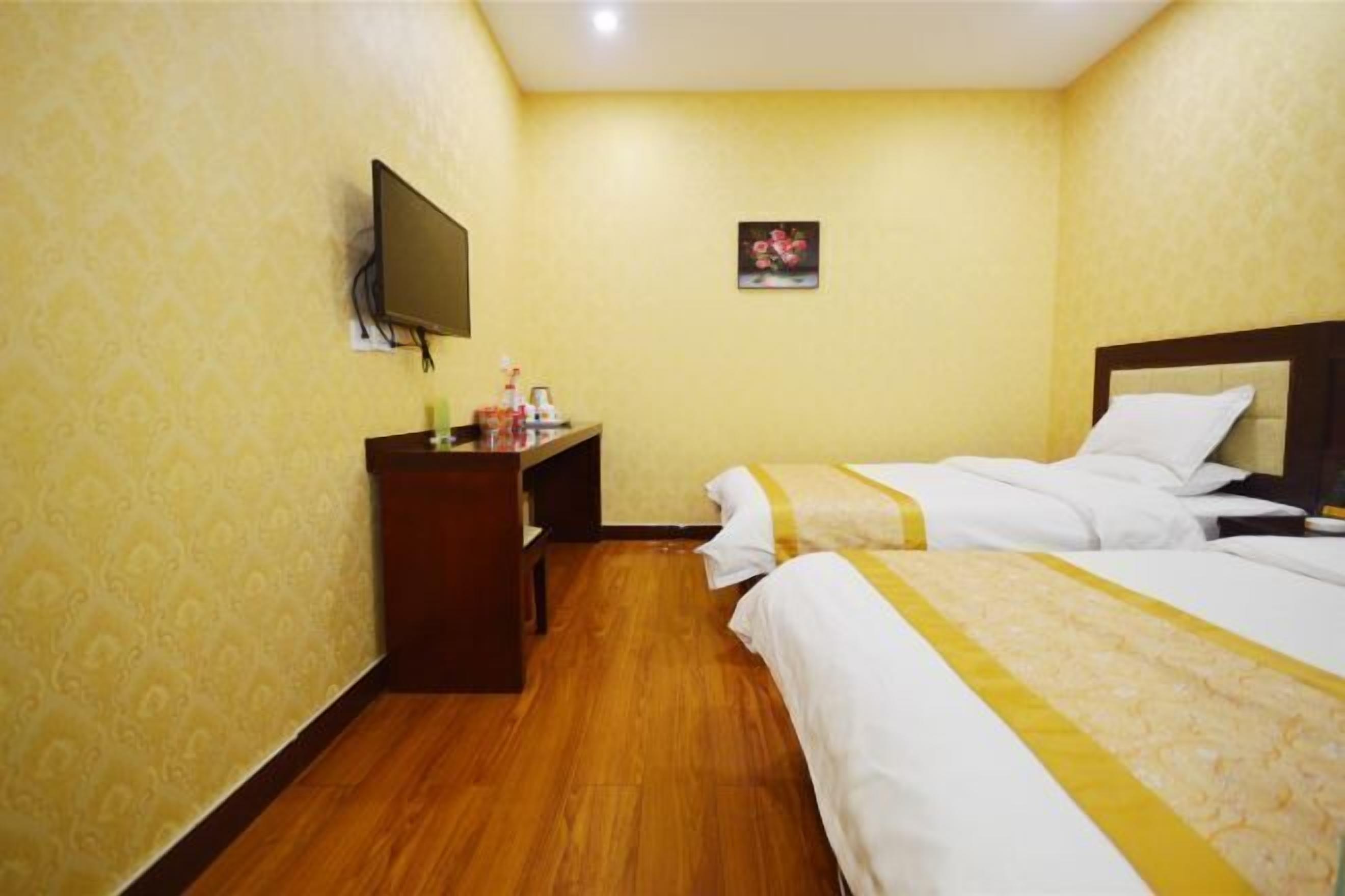 Quarto de hotel com duas camas, televisão, escrivaninha com luminária e uma pequena pintura na parede.