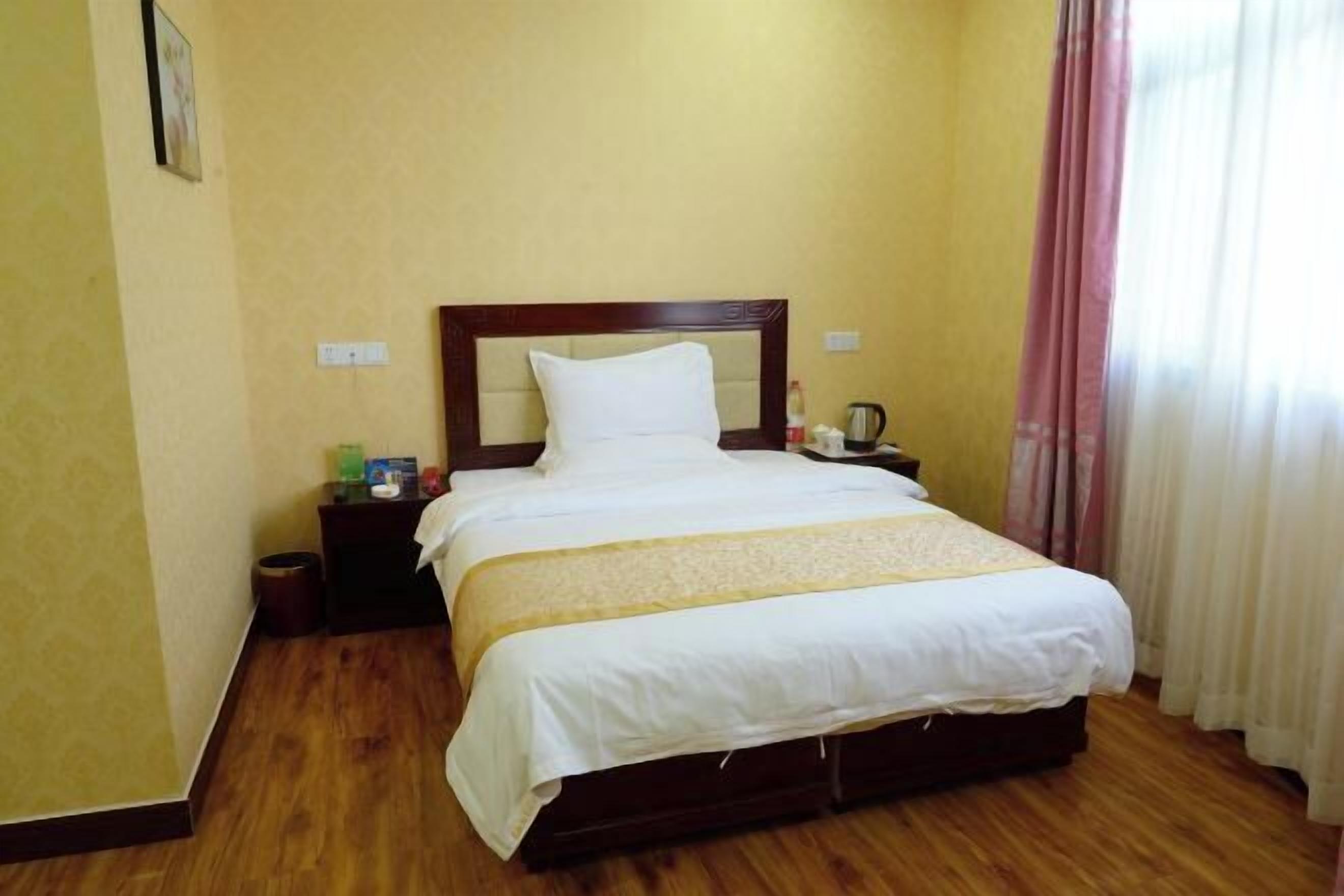 Een hotelkamer met een groot bed, houten vloer en nachtkastje met lamp.
