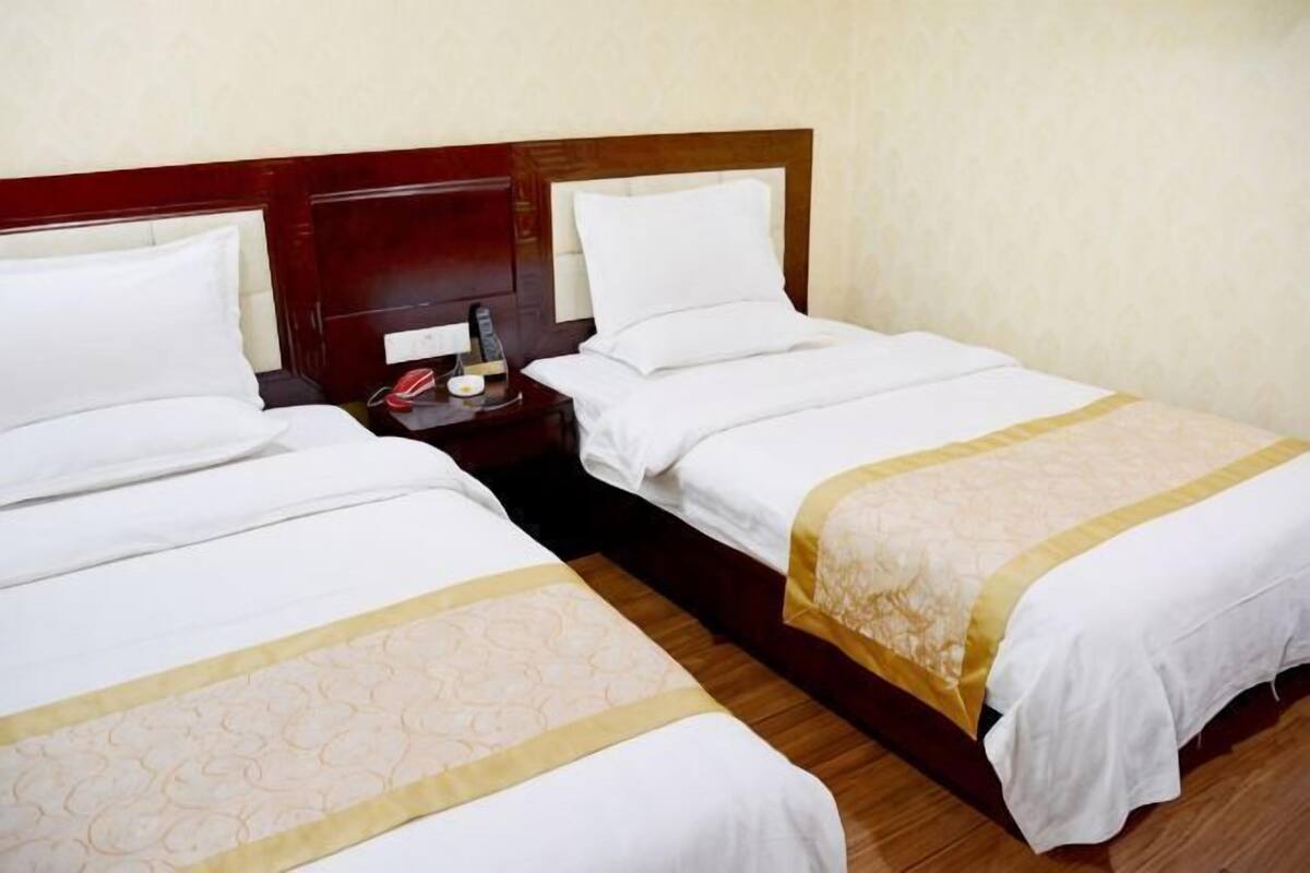 Two single beds with wooden headboards, white linens, and a small bedside table with a lamp.