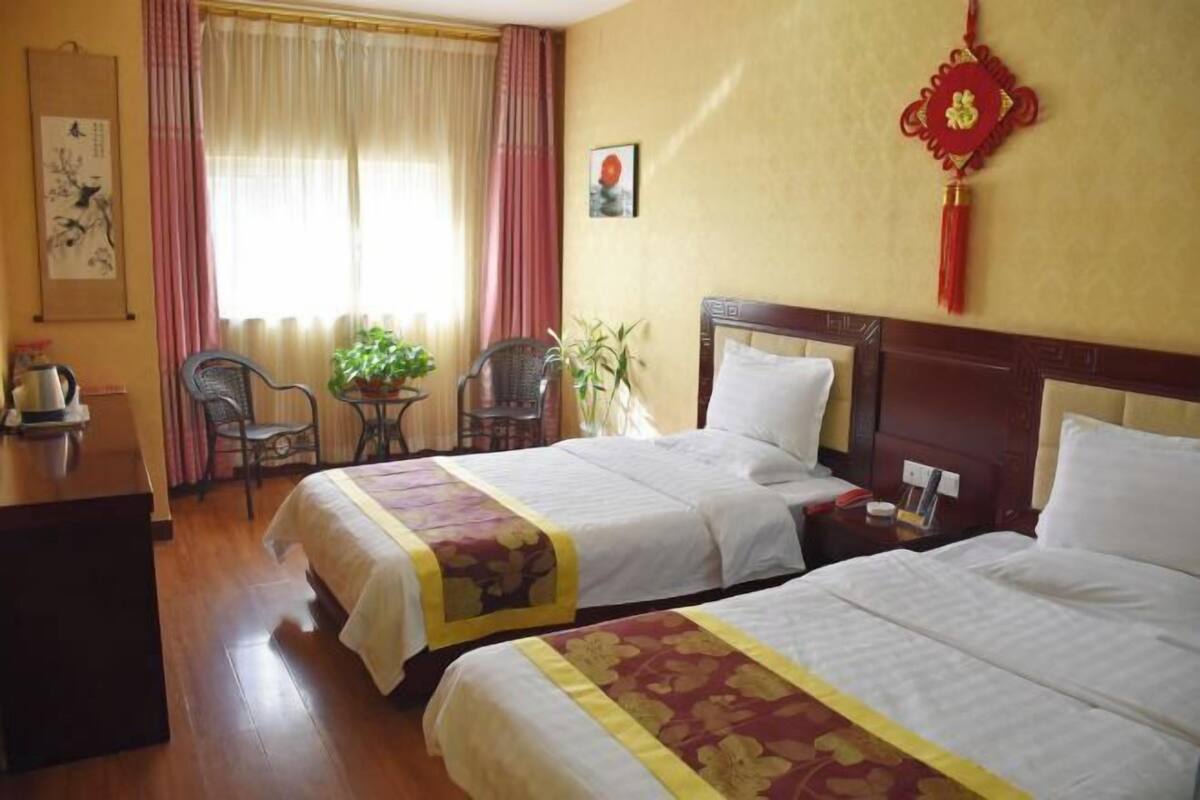 A hotel room with two beds, a desk, a chair, a table with a plant, and a window with curtains.