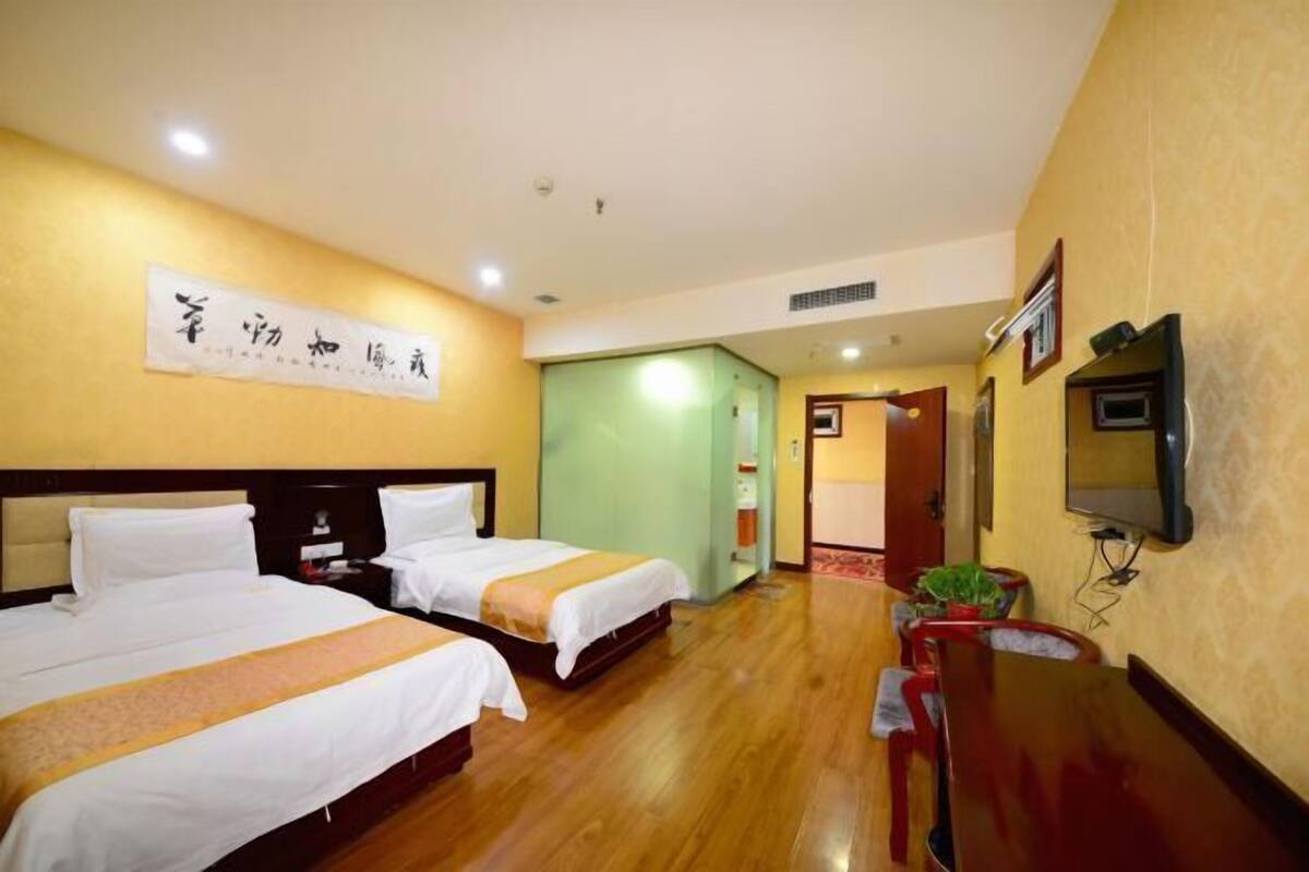 A hotel room with two beds, a television, a desk, and a door leading to another room.