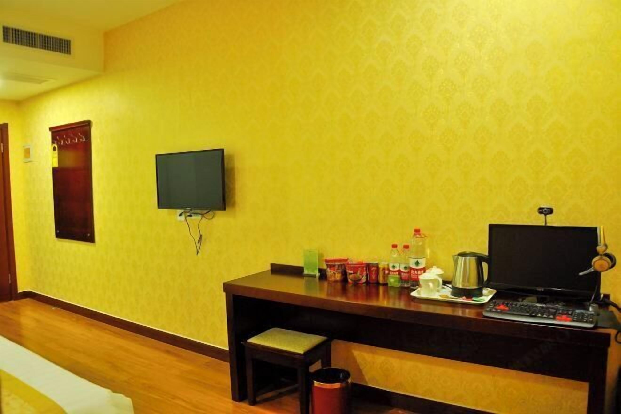 Habitación de hotel con un escritorio de madera, un televisor y varios objetos sobre el escritorio, incluyendo un ordenador portátil, una cafetera y algunos aperitivos.