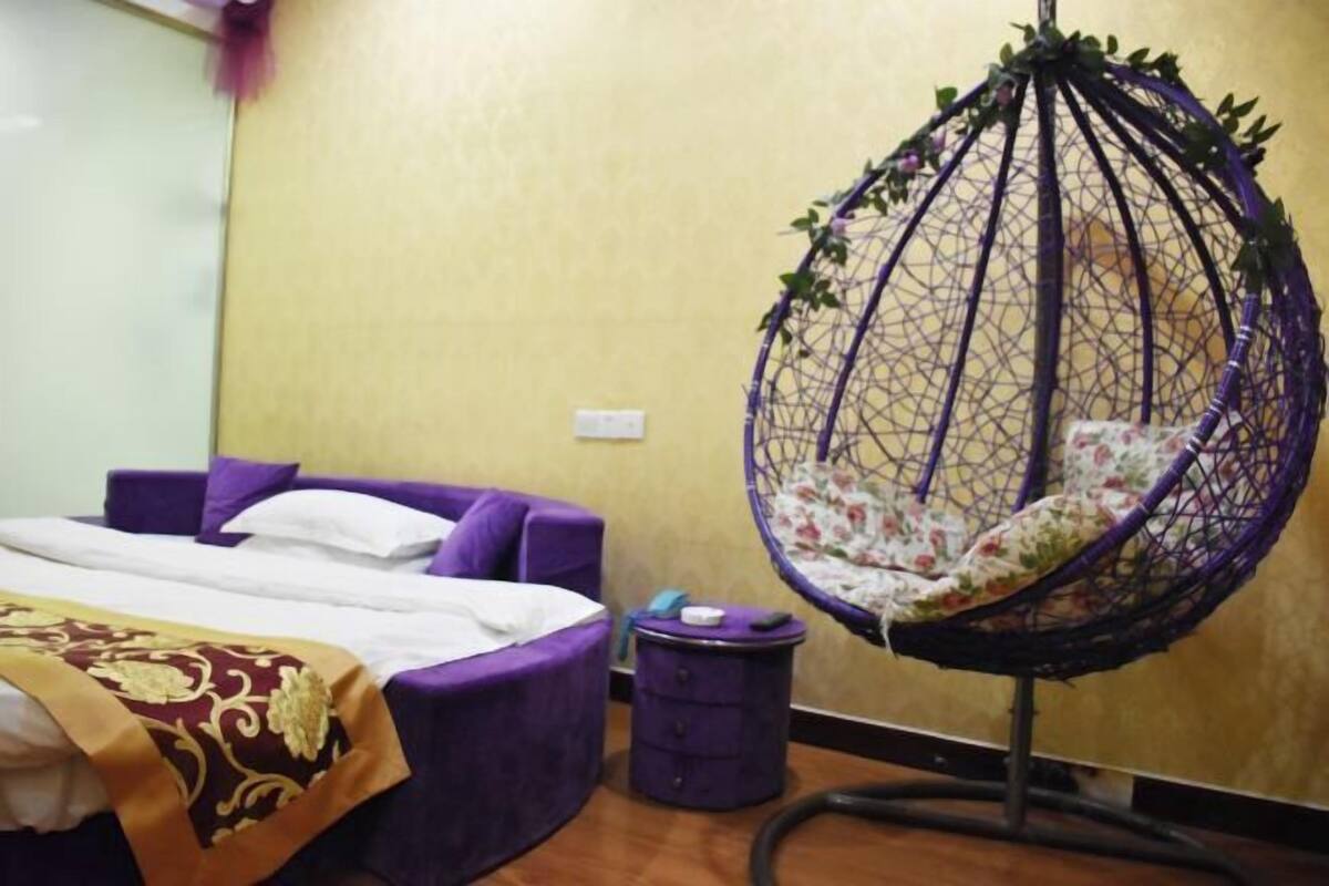 A room with a bed, a purple hanging chair, and a small trash bin.