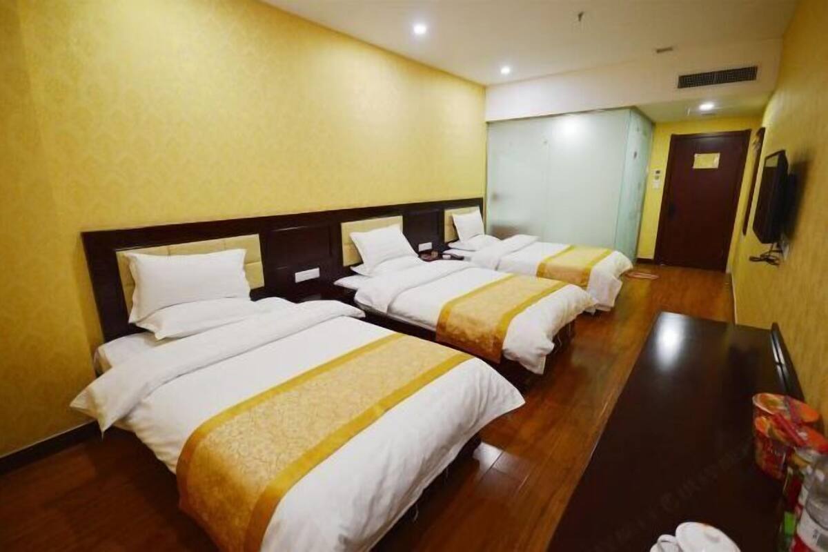 A hotel room with four single beds, wooden flooring, a dark wooden table, and a television on the wall.