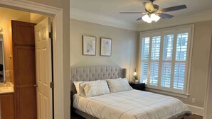 A bedroom with a tufted headboard, a large window with blinds, and a ceiling fan. - 1 Bdrm|Pet Friendly|North Hills|Long Stays (Raleigh)