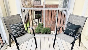 Two outdoor chairs with patterned cushions on a wooden deck, overlooking a brick building with a balcony. - 1 Bdrm|Pet Friendly|North Hills|Long Stays (Raleigh)