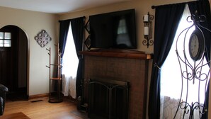 A living room with a fireplace, a television mounted above it, and a coat rack.