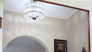 A living room with a wooden floor, a couch, a coffee table, and a chandelier. There is a dining area with a table and chairs in the background.
