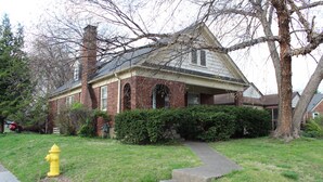 A two-story brick house with a chimney, a front yard with a yellow fire hydrant, and a sidewalk leading to the front door.