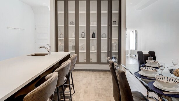Een moderne keuken met een centraal kookeiland, barstoelen en een eettafel voor zes personen.