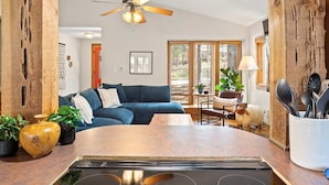 A modern kitchen with a central island, wooden beams, a ceiling fan, and a dining area with a table and chairs.