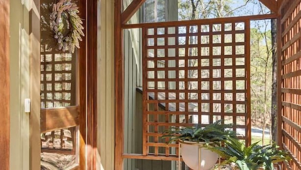 A wooden deck with a welcome mat, a lattice screen, and potted plants.