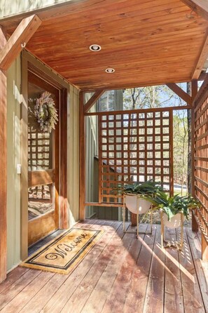 A wooden deck with a welcome mat, a lattice screen, and potted plants.