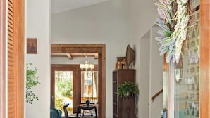 A wooden-floored hallway with a rug, a dining area with a table and chairs, and a large wooden cabinet.