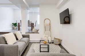Una sala de estar moderna con un sofá gris, una mesita de centro y un televisor montado en la pared.