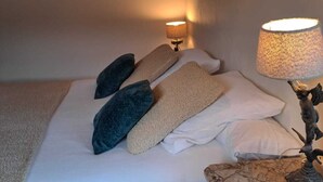 Een net opgemaakt bed met kussens, een lamp en een klein tafeltje met een decoratief object.