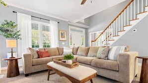 A living room with a beige sofa, a wooden coffee table, and a staircase. - Fenced In|Pets OK|By DT Apex|King Bed|EV Charger (Apex)