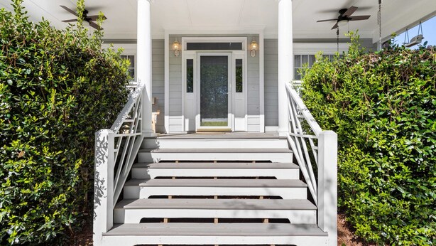 A grand staircase leading to a covered porch with columns and a door, flanked by lush greenery. - Fenced In|Pets OK|By DT Apex|King Bed|EV Charger (Apex)