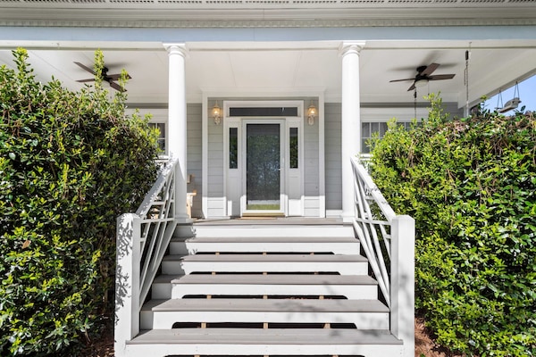 The wide front steps lead to a charming covered porch featuring classic white columns and cooling ceiling fans. It is a perfect spot for relaxing outdoors while enjoying the fresh air and neighborhood views.