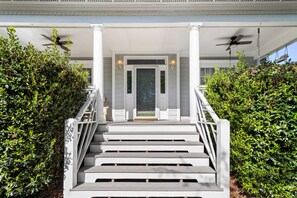 A grand staircase leading to a covered porch with columns and a door, flanked by lush greenery. - Fenced In|Pets OK|By DT Apex|King Bed|EV Charger (Apex)