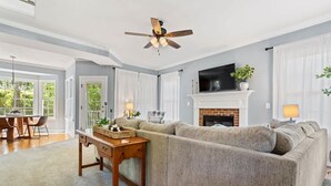 A living room with a sectional sofa, a fireplace, a ceiling fan, and a dining area with a table and chairs. - Fenced In|Pets OK|By DT Apex|King Bed|EV Charger (Apex)
