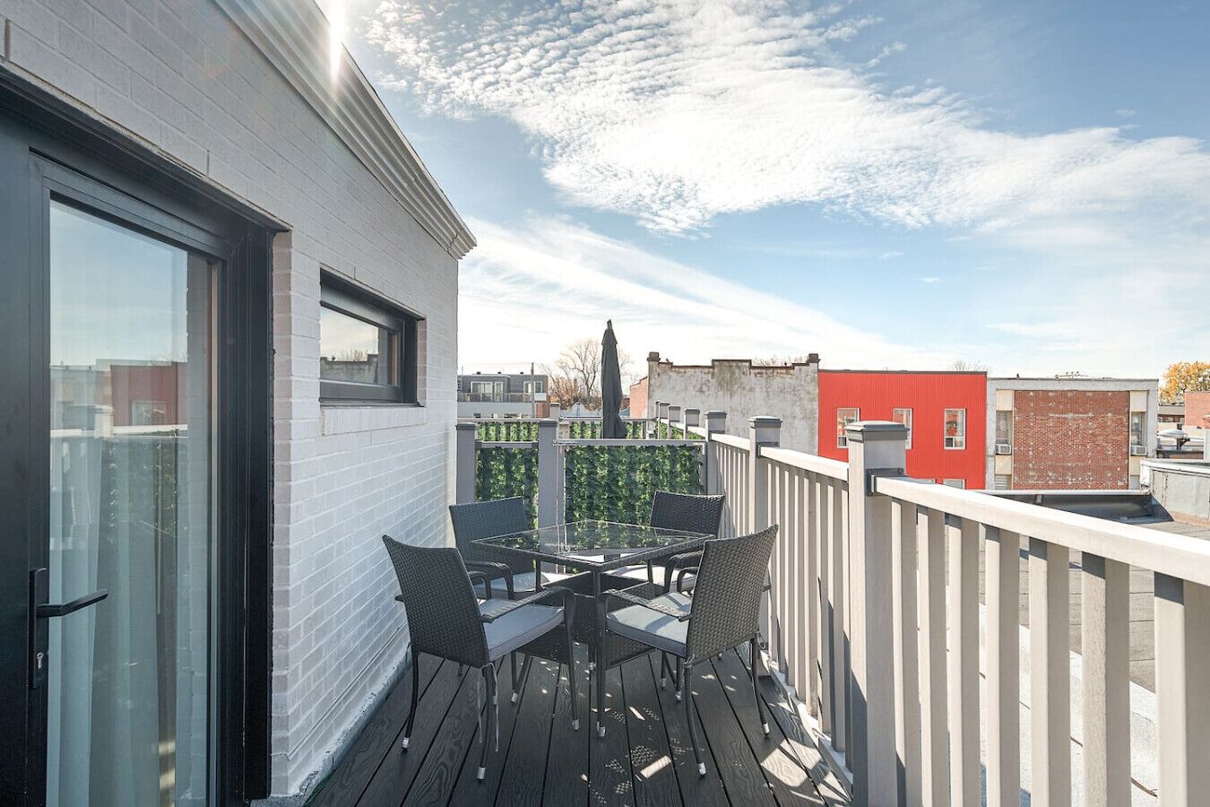 Un balcon avec une table et des chaises en verre, une balustrade blanche et une vue sur les bâtiments en arrière-plan.