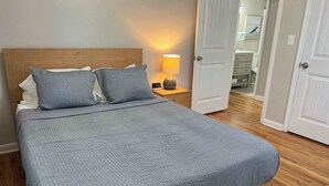 Un lit avec une couette grise, deux oreillers, une lampe de chevet et une table de nuit en bois.
