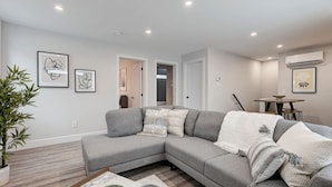 A modern living room with a grey sectional sofa, a dining table, and a potted plant.
