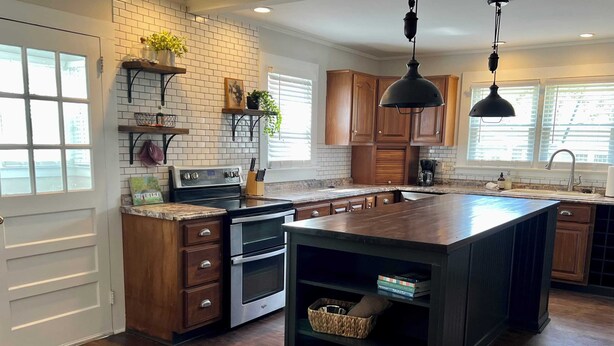 A modern kitchen with a large island, wooden cabinets, and a brick backsplash.