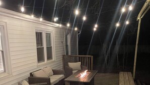 An outdoor deck with a fire pit, wicker furniture, and string lights.